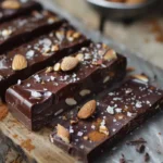 A close-up of a homemade chocolate bar with a glossy finish, topped with almonds and sea salt