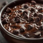 A creamy bowl of black bean brownie batter topped with chocolate chips and a drizzle of melted chocolate