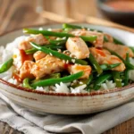 A plate of homemade string bean chicken with tender chicken strips, crisp green beans, and a savory sauce, served over white rice